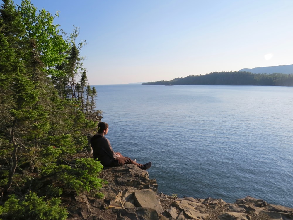 a man sitting on a cliff overlooking a body of water