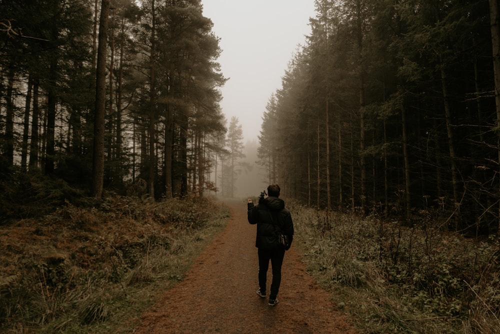 man in black jacket walking on dirt road between trees during daytime