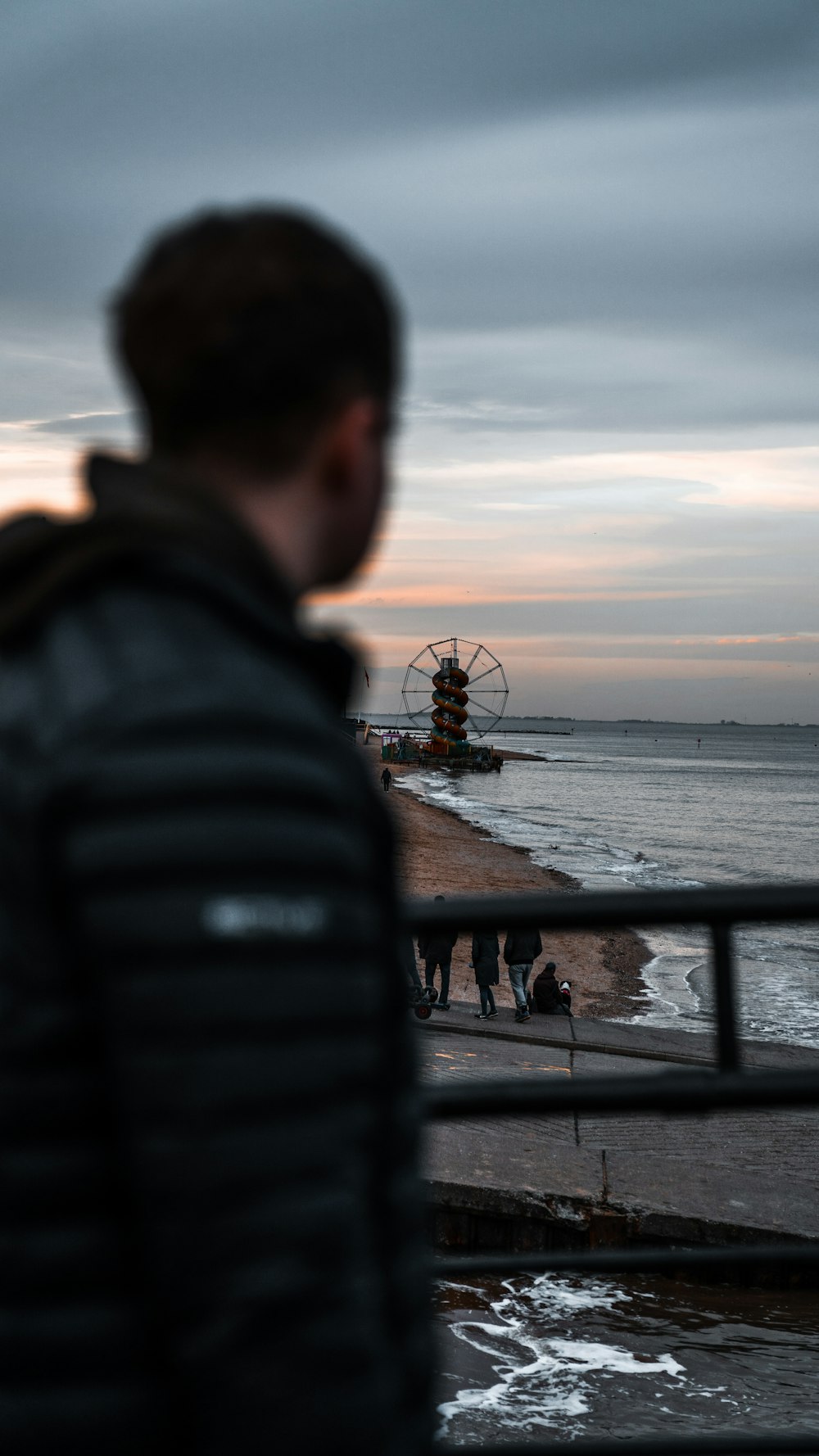 昼間、水辺に立つ黒いジャケットを着た男性