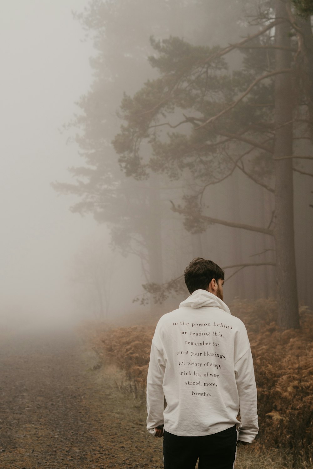 man in white dress shirt standing near bare trees covered with fog