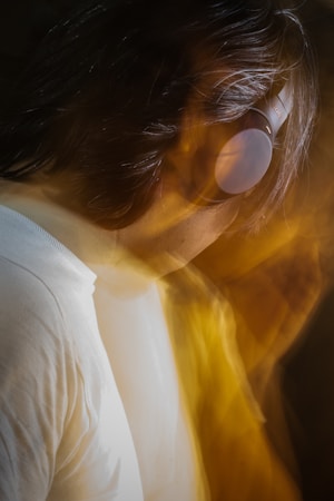 A person wearing headphones is featured with blurred motion effects, creating a dynamic and artistic visual. The background is dark, adding contrast to the motion blur of warm golden tones surrounding the subject.