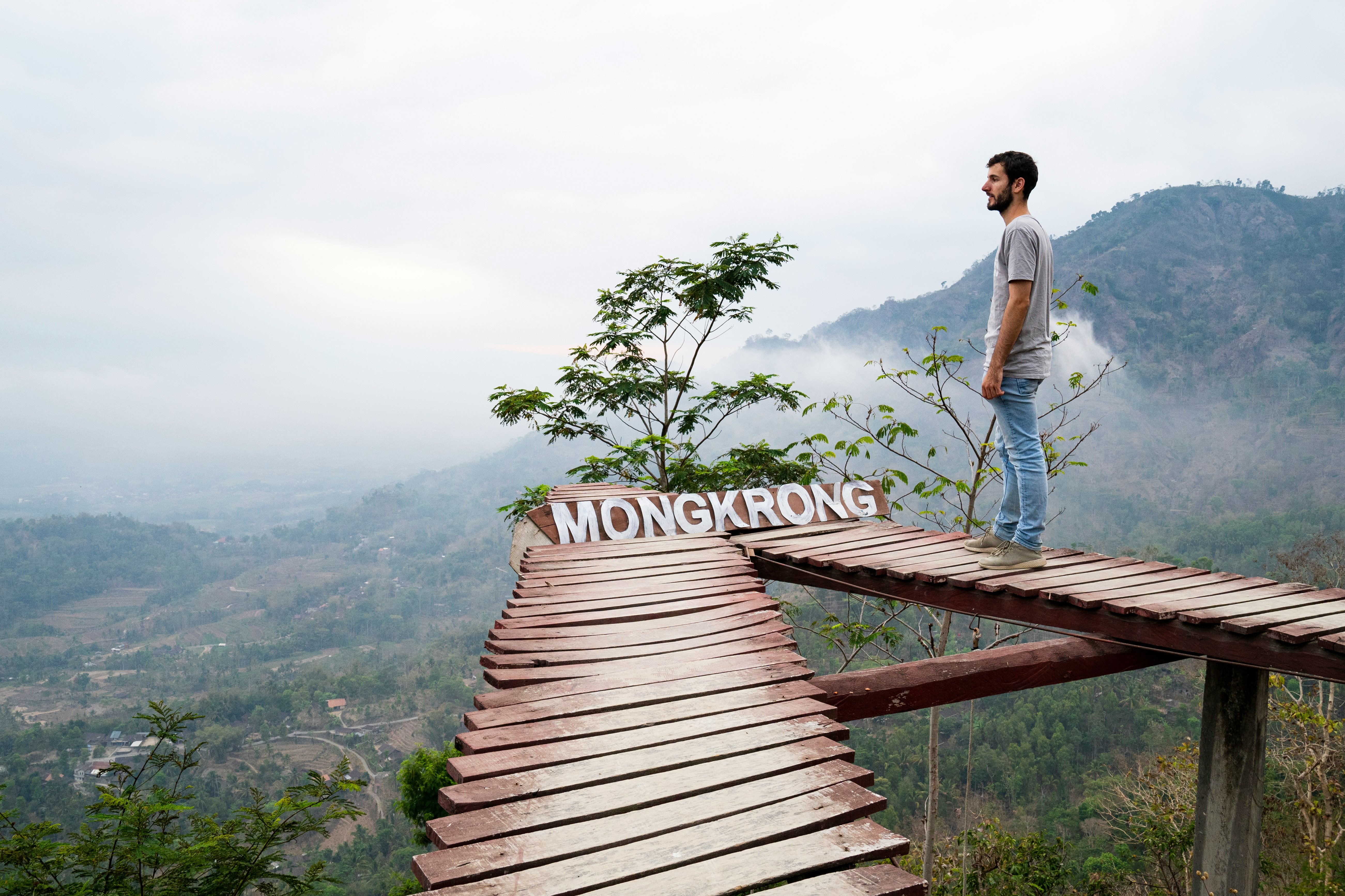 man in white t-shirt standing on brown wooden bridge during daytime