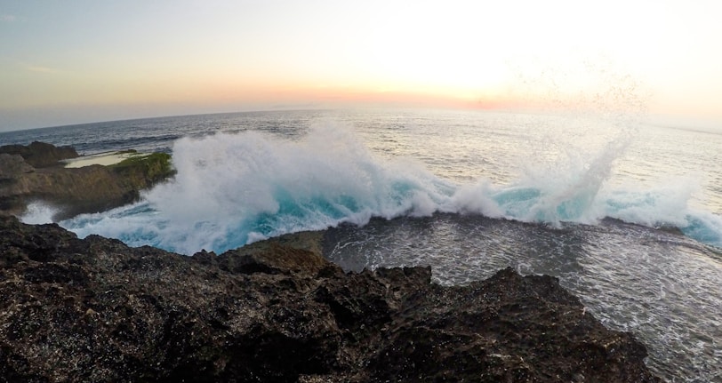 Ocean waves crashing against rocky cliffs during sunset.