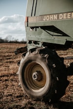 A close-up of a large agricultural machine with the branding visible, displaying sturdy tires resting on a grassy field under a partly cloudy sky. The machinery appears robust, equipped for fieldwork.
