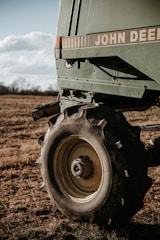 A close-up of a large agricultural machine with the branding visible, displaying sturdy tires resting on a grassy field under a partly cloudy sky. The machinery appears robust, equipped for fieldwork.