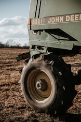 A close-up of a large agricultural machine with the branding visible, displaying sturdy tires resting on a grassy field under a partly cloudy sky. The machinery appears robust, equipped for fieldwork.