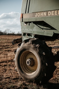 A close-up of a large agricultural machine with the branding visible, displaying sturdy tires resting on a grassy field under a partly cloudy sky. The machinery appears robust, equipped for fieldwork.