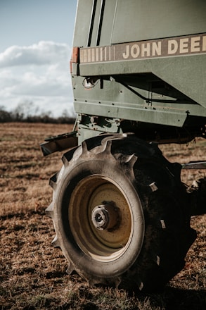 A close-up of a large agricultural machine with the branding visible, displaying sturdy tires resting on a grassy field under a partly cloudy sky. The machinery appears robust, equipped for fieldwork.