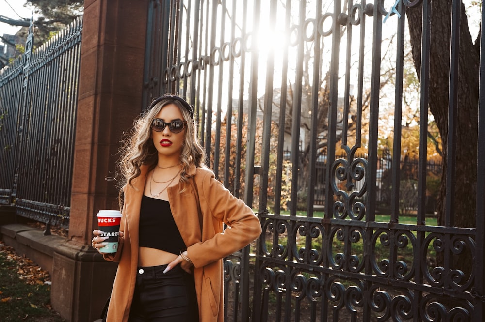 woman in brown coat standing beside black metal gate