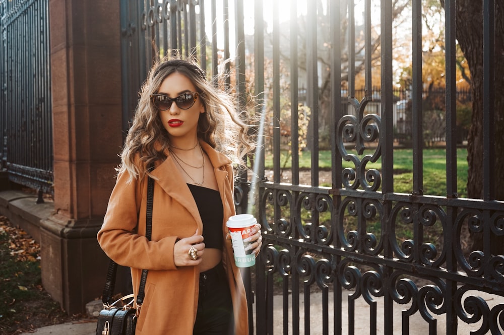 woman in brown coat holding white cup