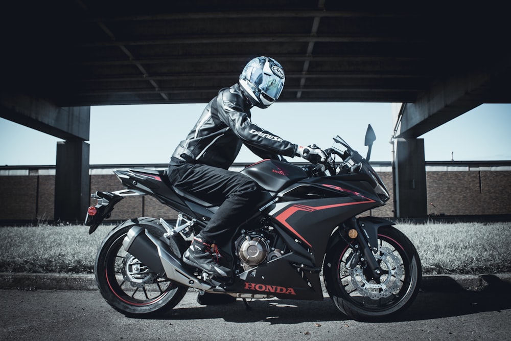 man in black leather jacket riding black and red sports bike