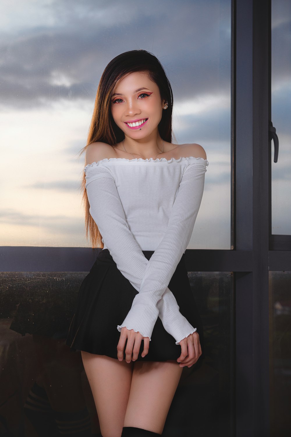 woman in white long sleeve shirt and black skirt sitting on window during daytime