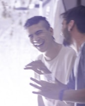Two people are engaged in a moment of laughter and conversation. One is holding a drink and gesturing with their hands, while the other appears to be mid-laugh. The image is slightly blurred, giving it a dynamic and candid feel.
