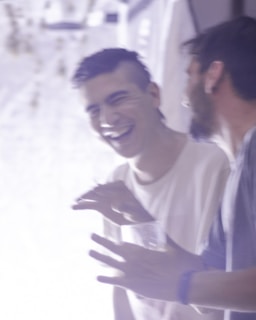 Two people are engaged in a moment of laughter and conversation. One is holding a drink and gesturing with their hands, while the other appears to be mid-laugh. The image is slightly blurred, giving it a dynamic and candid feel.