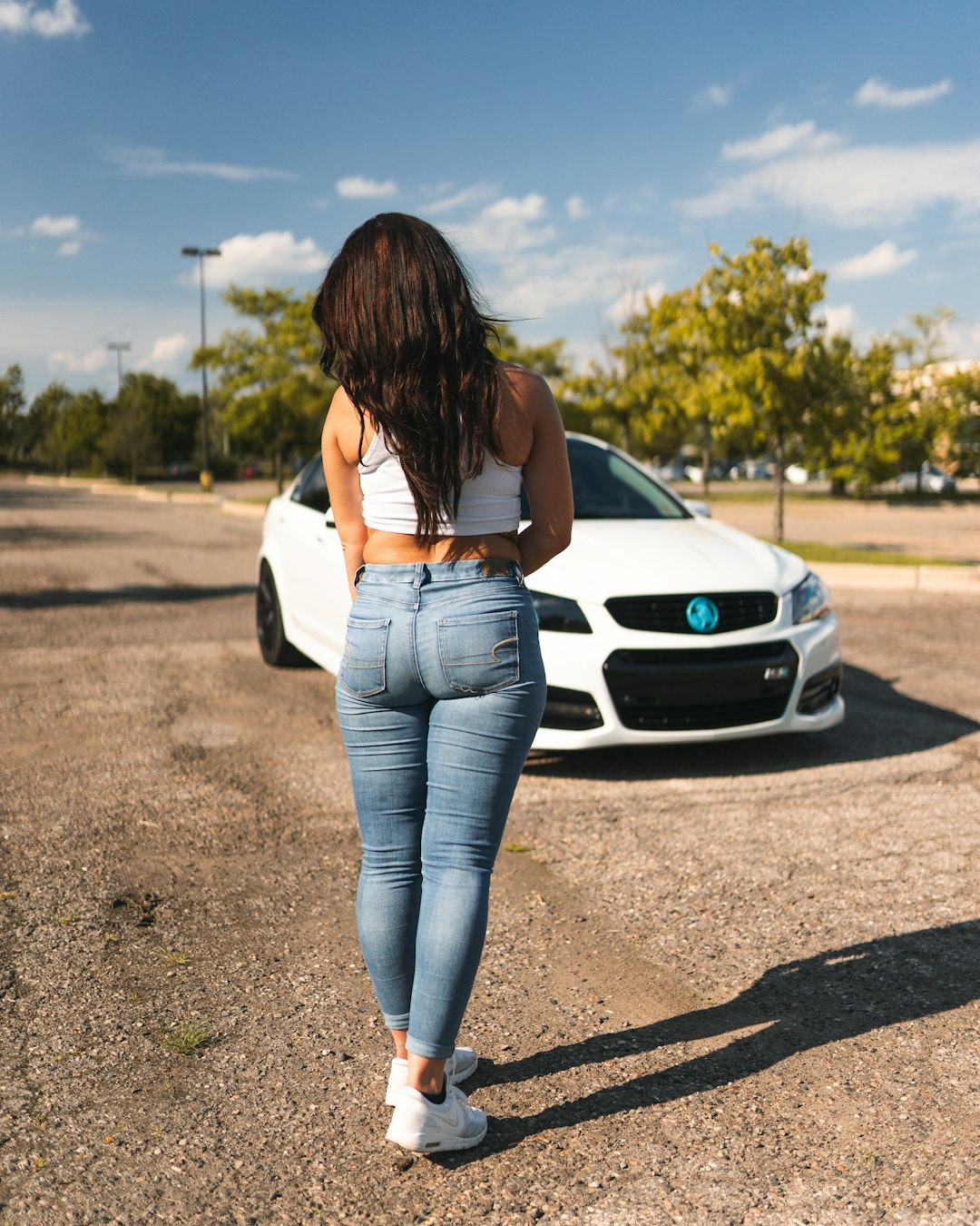 woman in white long sleeve shirt and blue denim jeans standing beside white car during daytime