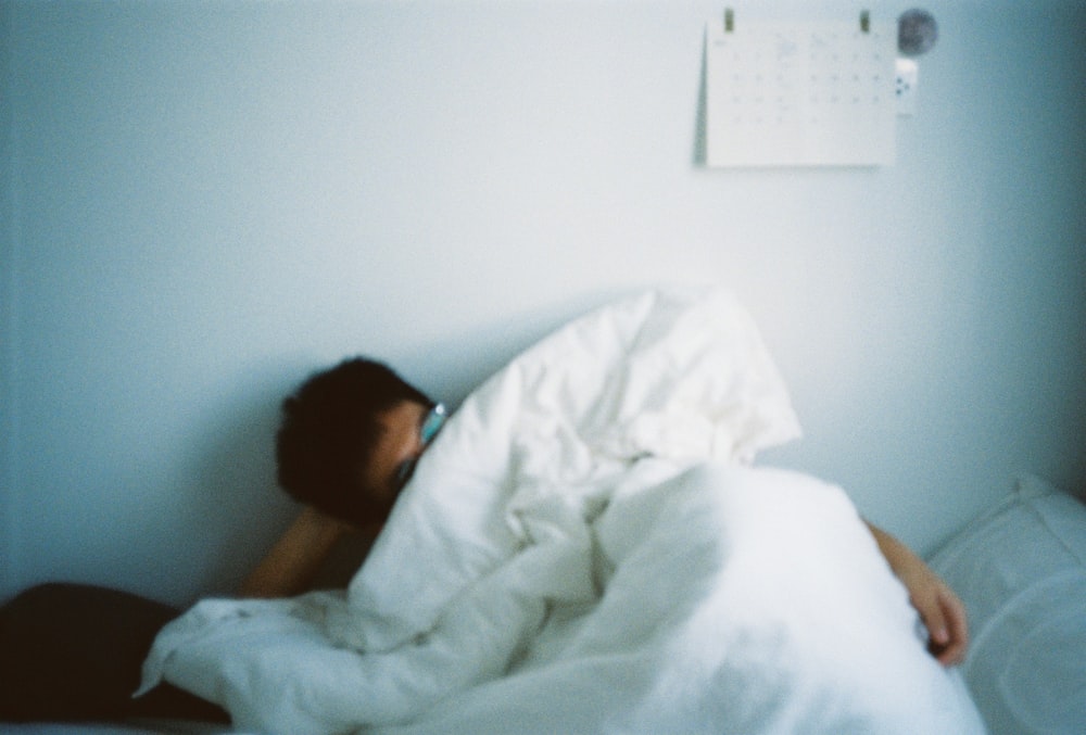 woman lying on bed covered with white blanket