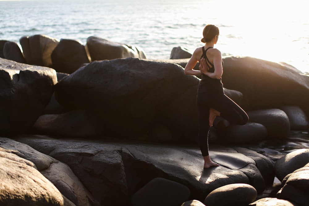 woman in black bikini standing on rock near sea during daytime