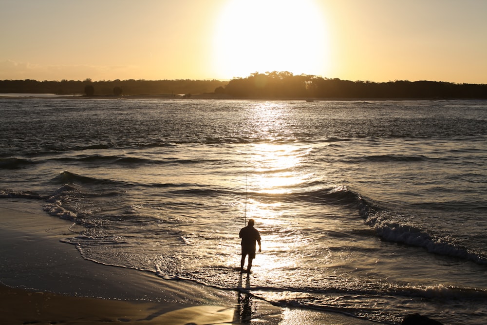 silhouette de personne debout sur le bord de mer pendant le coucher du soleil