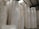 Large rolls of paper are stacked in a warehouse setting with high ceilings and exposed beams. The rolls are uniformly white and cylindrical, arranged in tall columns.