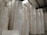 Large rolls of paper are stacked in a warehouse setting with high ceilings and exposed beams. The rolls are uniformly white and cylindrical, arranged in tall columns.