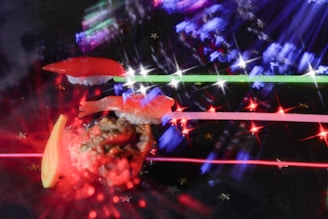 A vibrant and artistic arrangement featuring sushi pieces, such as nigiri and a sushi roll, set against a dark background with colorful light effects. The light creates a dynamic and abstract appearance, with streaks of red, blue, and green and sparkling star-like points.