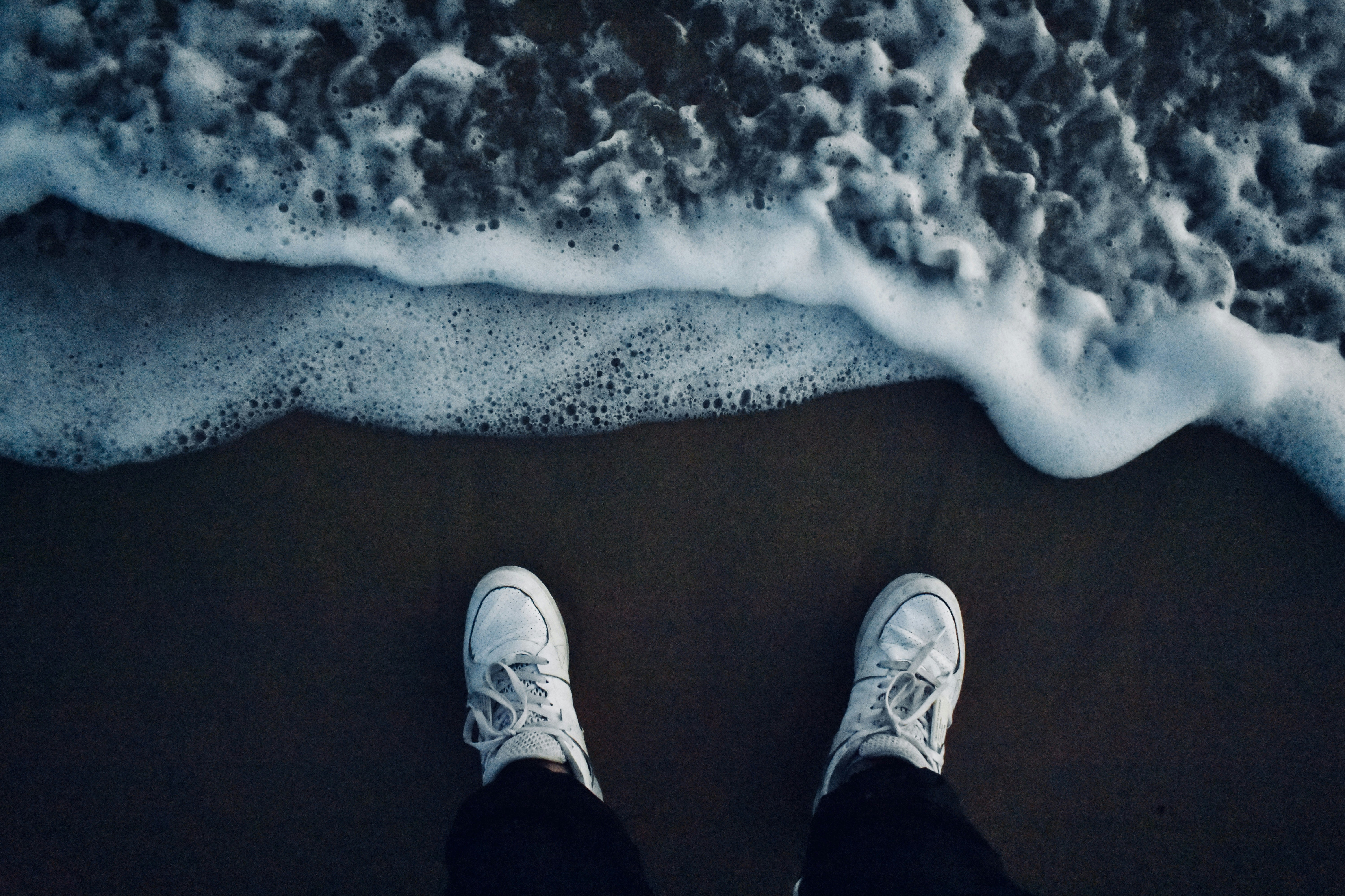 person in black pants and white sneakers standing on brown sand, 