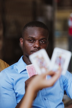 A person wearing a blue shirt is focused intently on playing cards held by someone else. The image highlights a mix of concentration and strategic thinking in a casual setting.