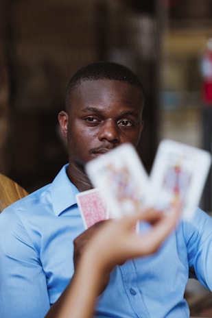 A person wearing a blue shirt is focused intently on playing cards held by someone else. The image highlights a mix of concentration and strategic thinking in a casual setting.