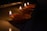 A row of lit oil lamps, known as diyas, is placed on a flat surface in a dimly lit environment. The flames flicker gently, casting a warm glow and creating a serene and peaceful atmosphere.