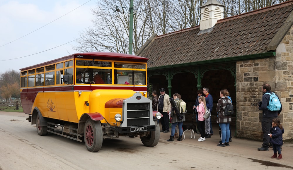people standing beside yellow and red bus during daytime