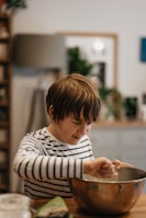A child helping a parent mix oils in a small bowl.