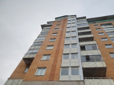 A tall, multi-story residential building with a combination of yellow and red brickwork along with glass balconies. The building features large, rectangular windows and has a modern architectural design.