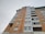 A tall, multi-story residential building with a combination of yellow and red brickwork along with glass balconies. The building features large, rectangular windows and has a modern architectural design.
