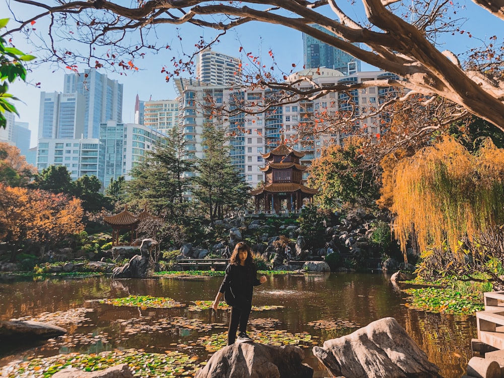 woman in black dress standing on brown wooden log near river during daytime