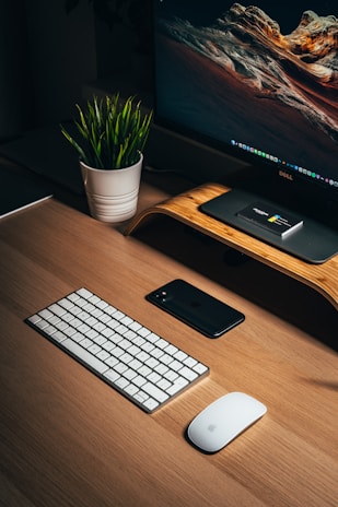A neat desk arrangement featuring a wooden monitor stand, a potted succulent, and a notebook beside a softly glowing lamp.