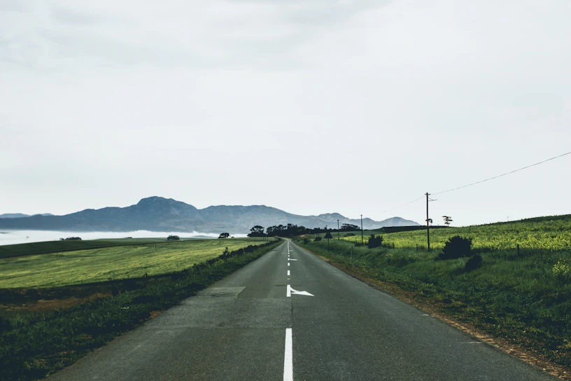 gray asphalt road between green grass field under white sky during daytime
