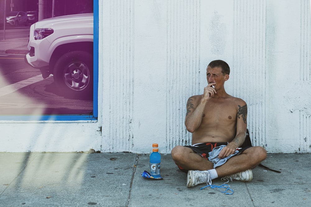 topless man sitting on floor beside blue and white plastic bottle