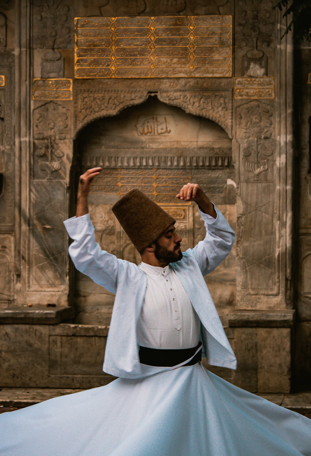 man in white long sleeve shirt wearing brown hat standing in front of brown concrete wall