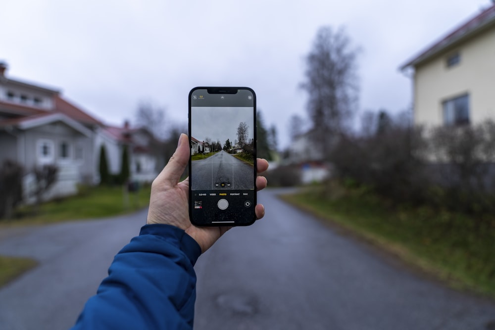 Persona che tiene l'iphone 5 nero che scatta foto della strada durante il giorno