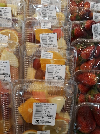 Plastic containers hold mixed fruit slices such as pineapples, oranges, and grapes, next to packages of fresh strawberries. Price labels indicate the cost per kilogram and emphasize immediate consumption.