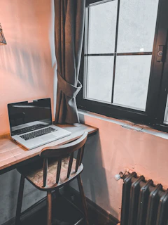 Compact desk made of light wood placed near a bright window.