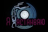 A neon sign featuring a stylized vinyl record with a tonearm and text in Cyrillic script. The sign uses vibrant blue and pink colors against a black background, creating a visually striking and retro aesthetic. The words 'бар', 'еда', and 'атмосфера' are written on the record label, hinting at a bar, food, and atmosphere theme.