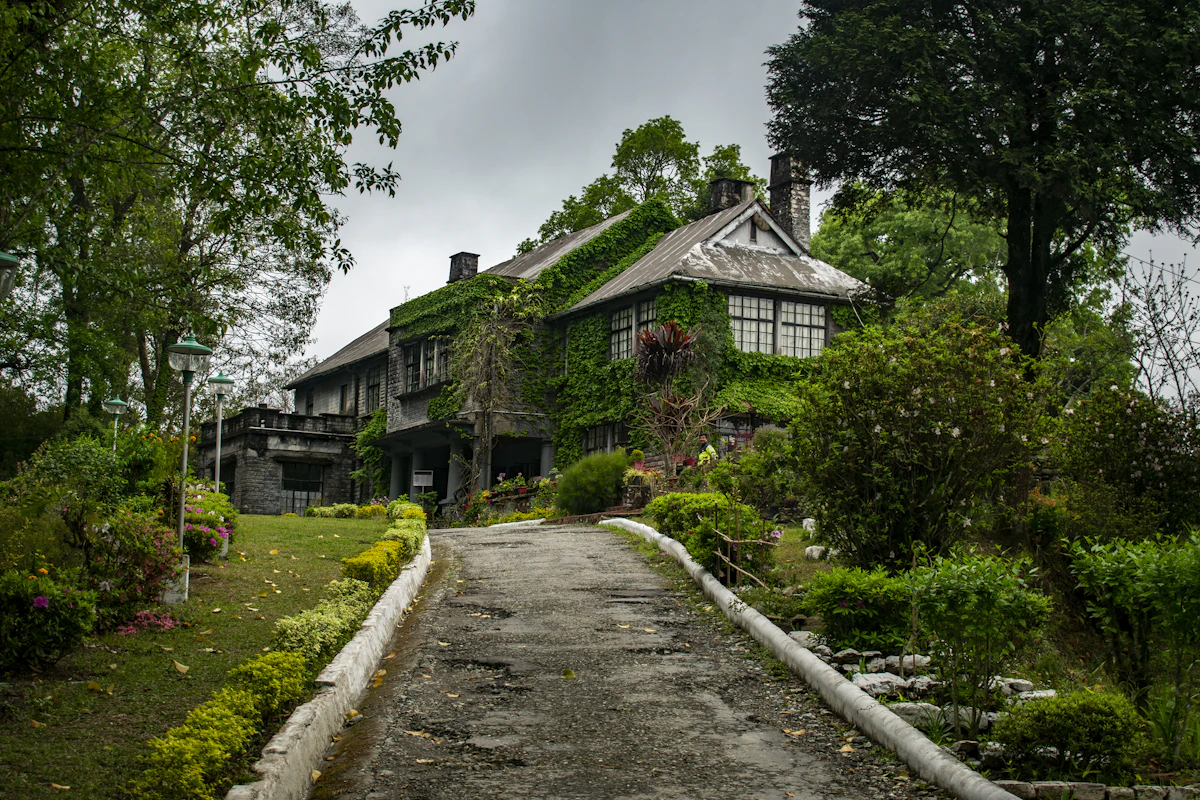 An ivy covered colonial stone bungalow in Kalimpong at the top of a hedge lined drive under grey cloud