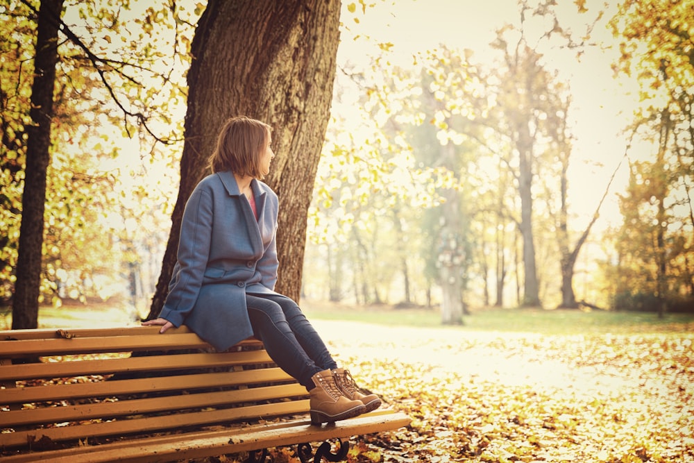 woman in blue blazer sitting on brown wooden bench during daytime