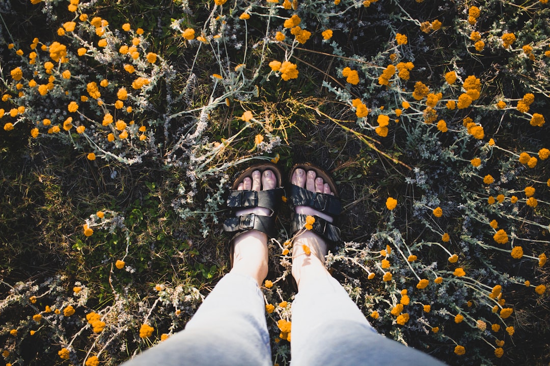 person in blue denim jeans and black hiking sandals standing on yellow leaves