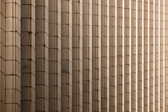 Rows of vertically aligned rectangular panels create a repetitive, symmetrical pattern. The panels are made of a beige or light brown material and seem to form part of a large architectural facade.