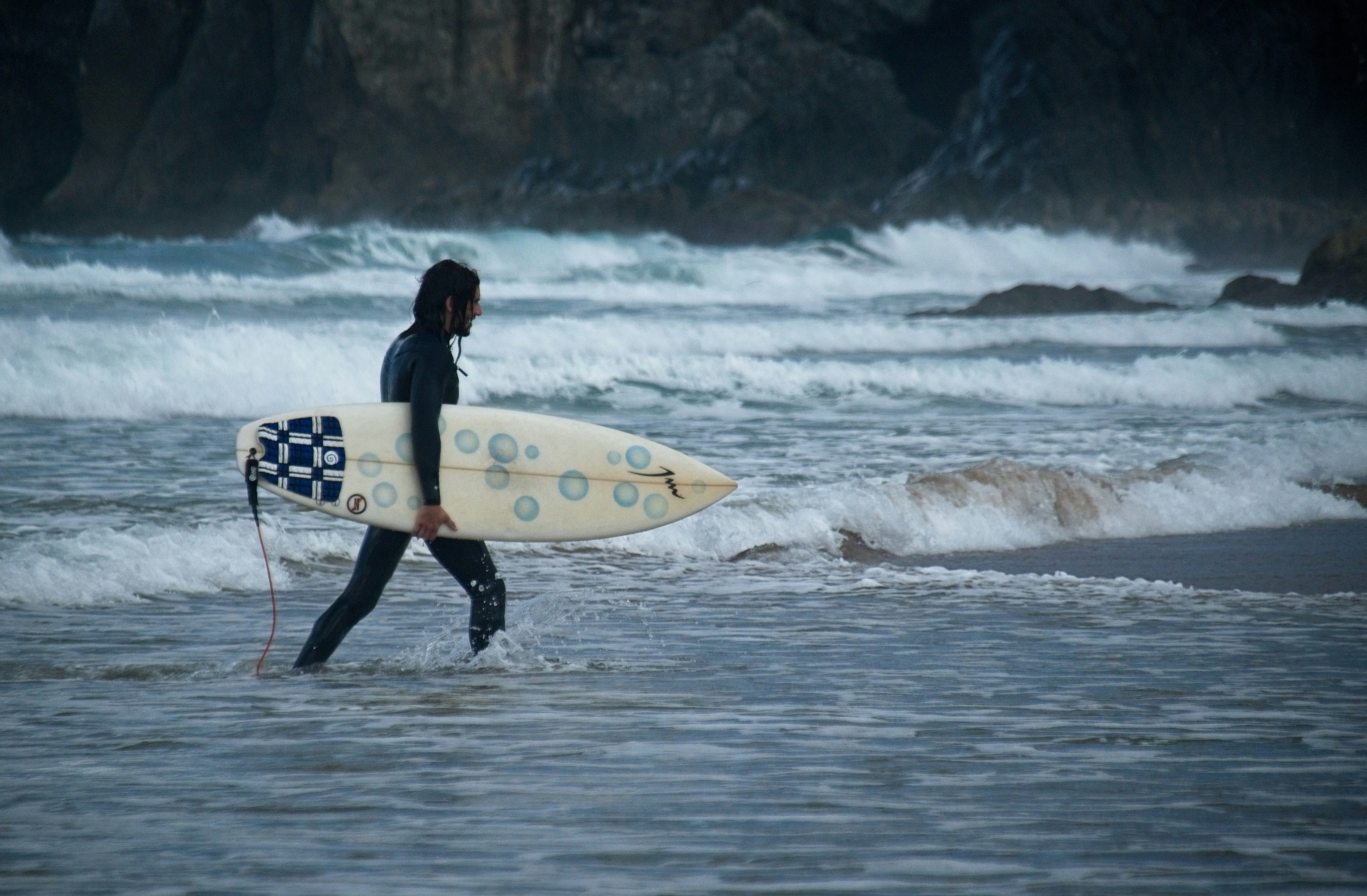man in black wet suit holding white surfboard walking on beach during daytime