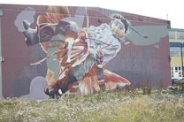 A large mural on the side of a building depicts a child with braided hair riding a giant fish. The artwork is vibrant and dynamic, covering the building facade with intricate details and bold colors.