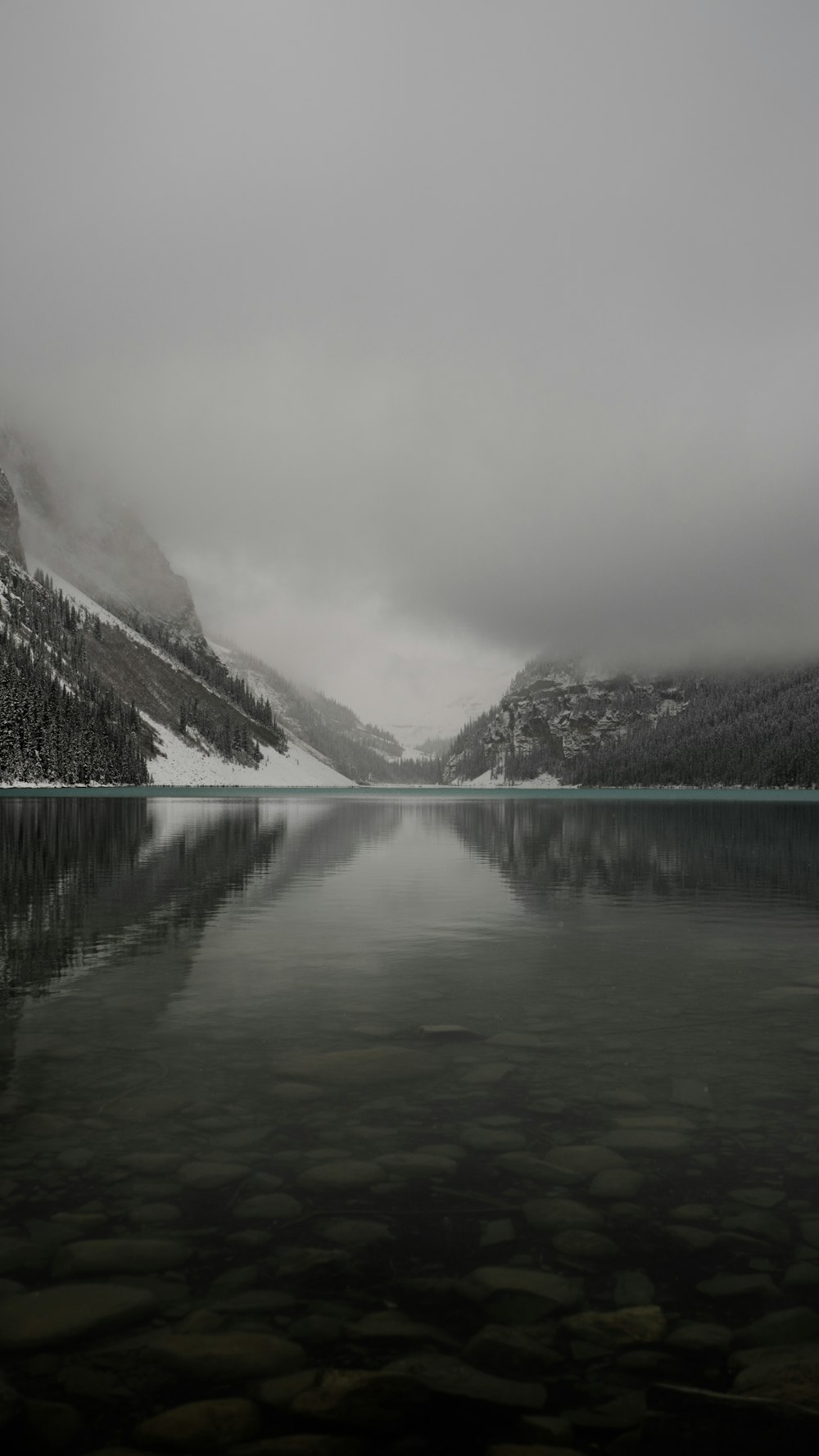 lake near mountain under white sky during daytime