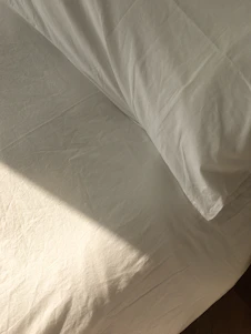 A serene bedroom bathed in morning light featuring a neatly made bed with beige and sand-colored washed cotton bedding.